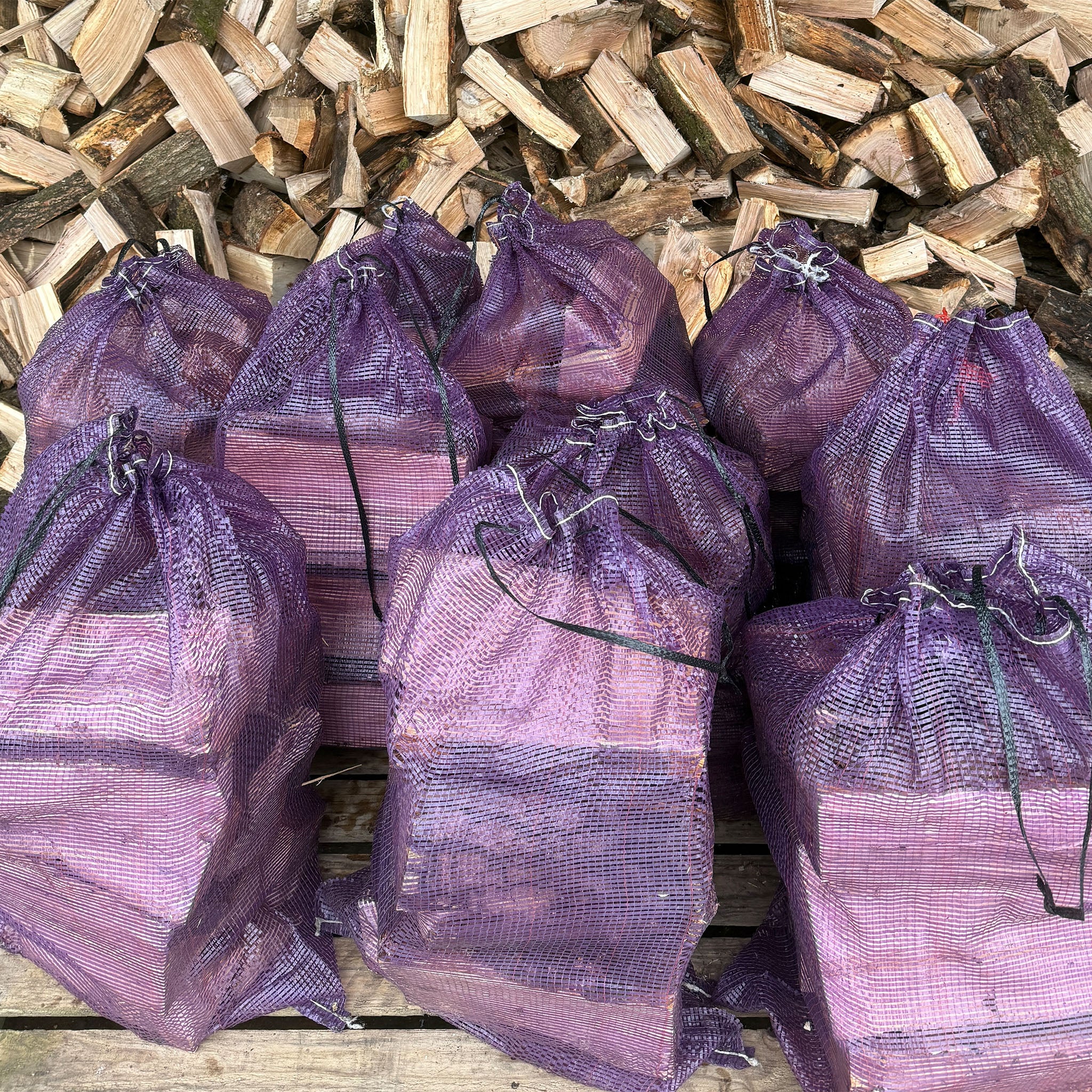 Purple mesh bags filled with firewood on a wooden pile