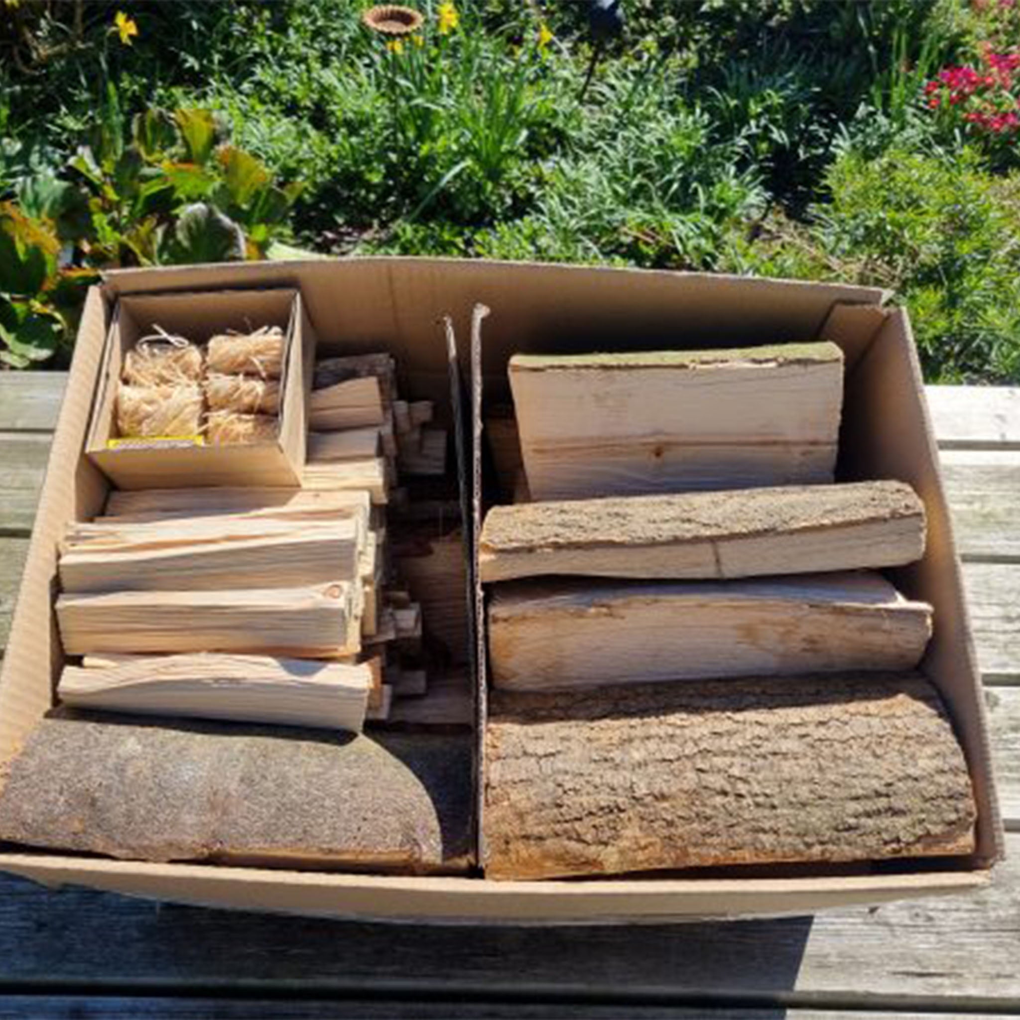 Box of firewood on a wooden surface with greenery in the background