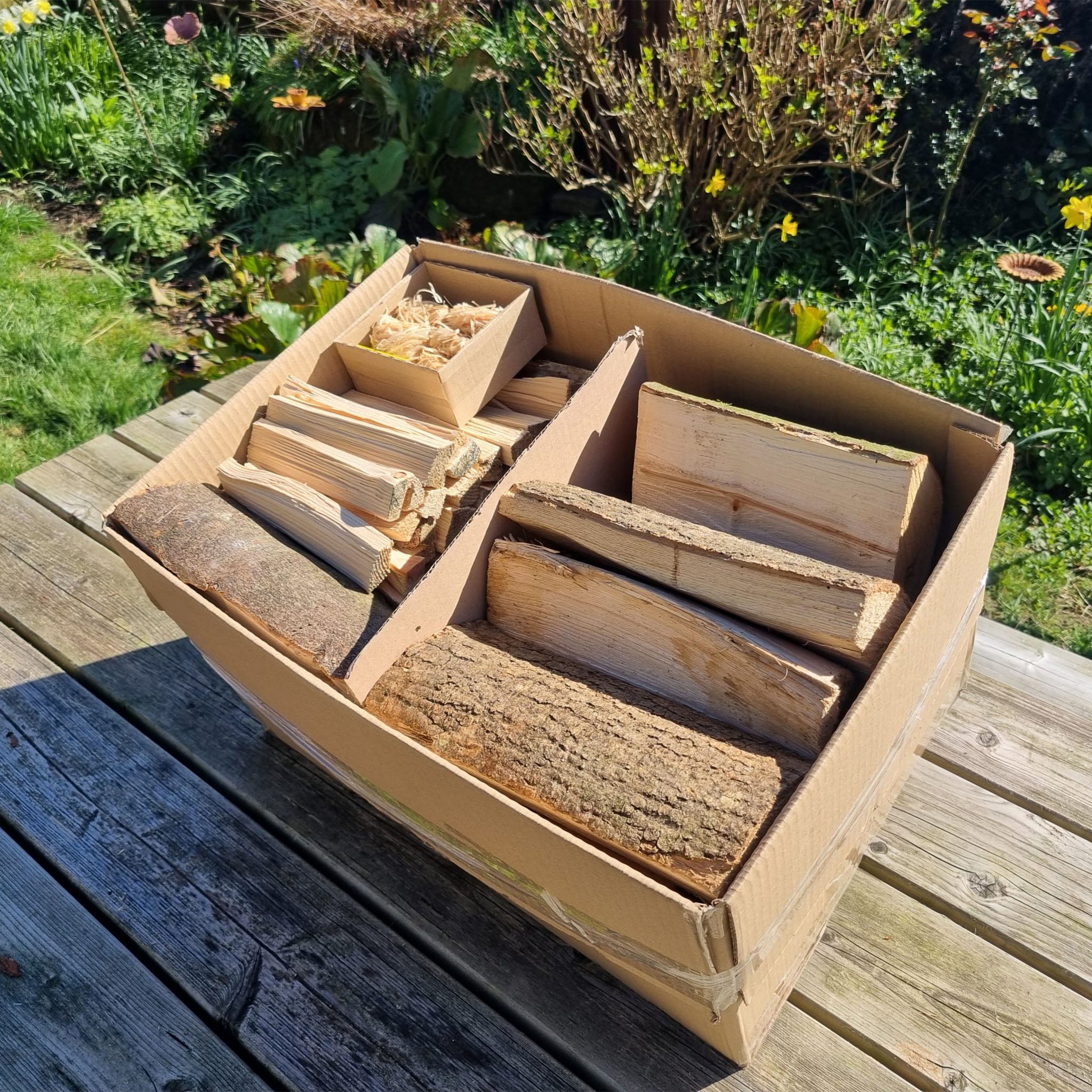 Box of wooden firewood logs on a wooden surface with a garden background
