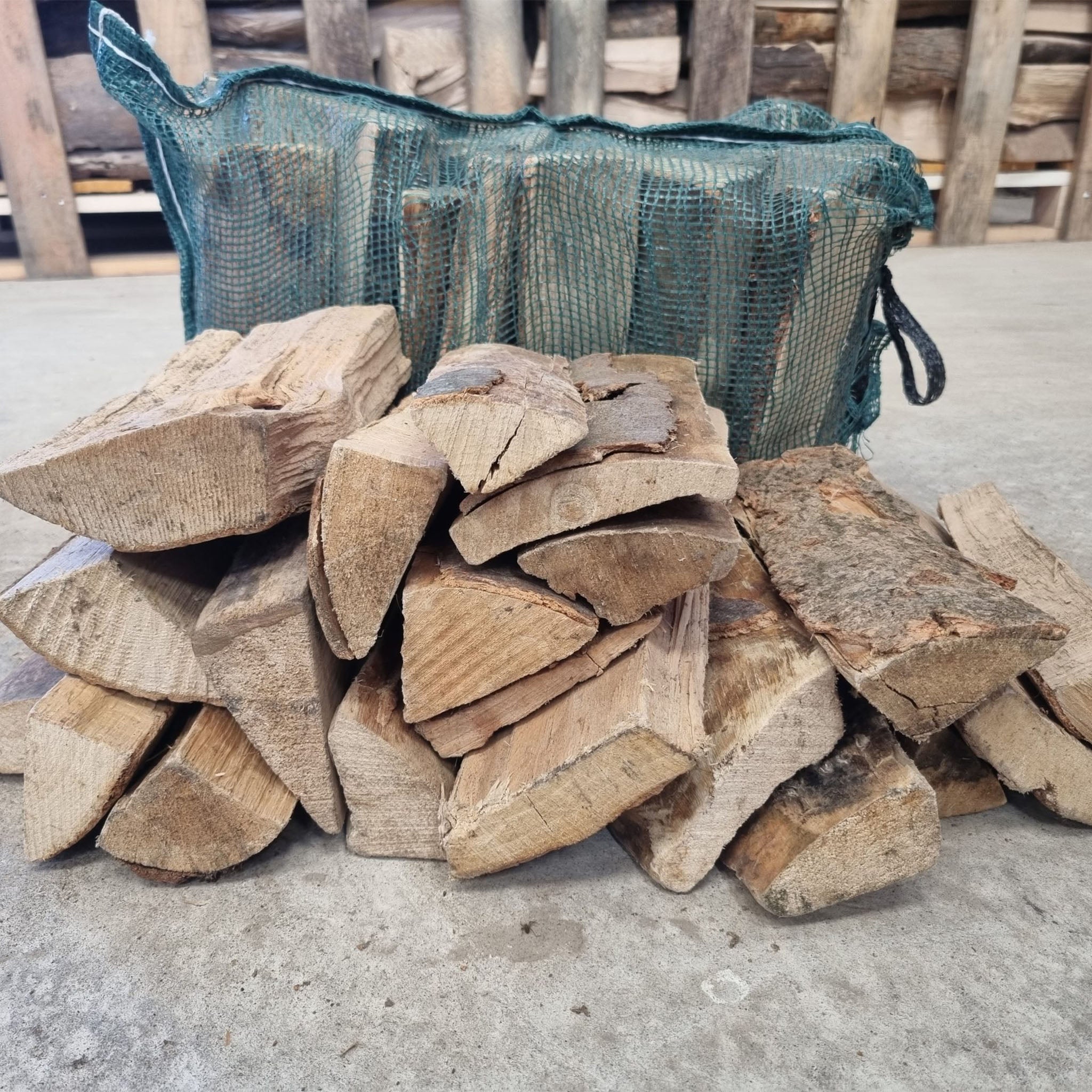 Stack of firewood with a green mesh bag in the background